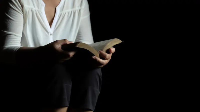 Hand resting on an open Bible with Acts 23:11 highlighted, lit gently in a dark room.