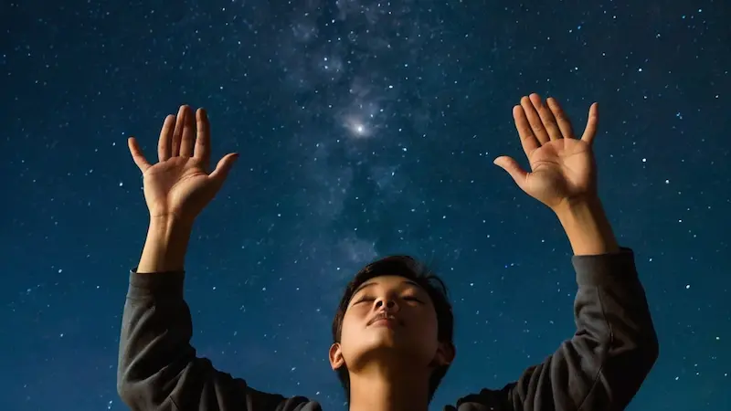 Hands lifted to heaven at night in prayer.