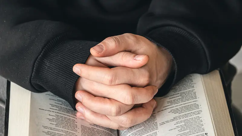 Open Bible with highlighted verses and a hand in prayer.