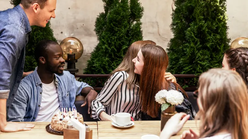 Group of young adults sitting together in a coffee shop, talking and laughing