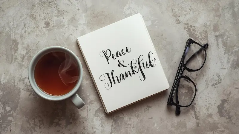 Open journal with “Peace” and “Thankful” written, beside tea and glasses