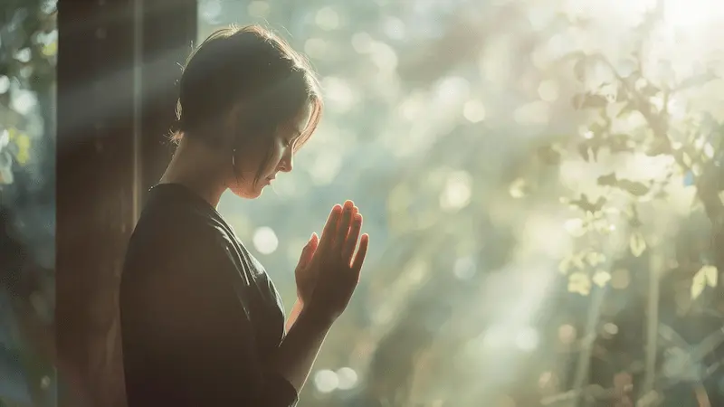 Person sitting in quiet prayer by a window with light streaming in