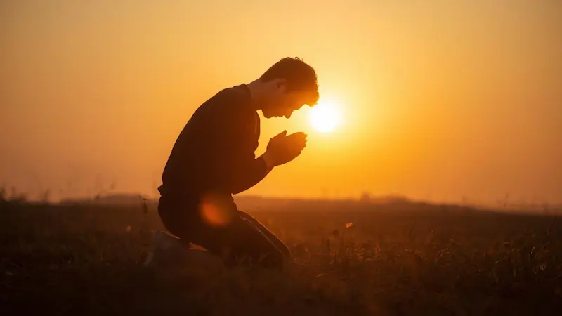 Person kneeling in dawn light, symbolizing steadfast prayer and trust in God