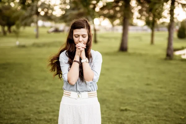 Woman praying outdoors at sunrise reflecting on God’s faithfulness.”