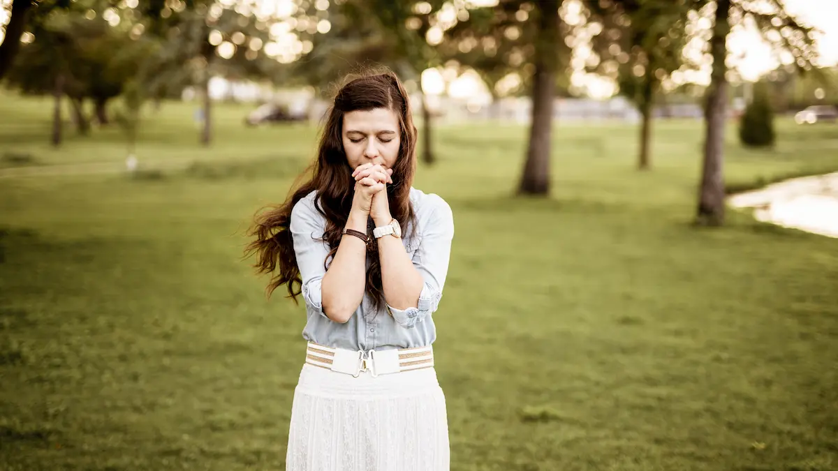 Woman praying outdoors at sunrise reflecting on God’s faithfulness.”