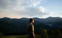 "Man standing in rural countryside with arms lifted in surrender, embracing peace and connection with God"