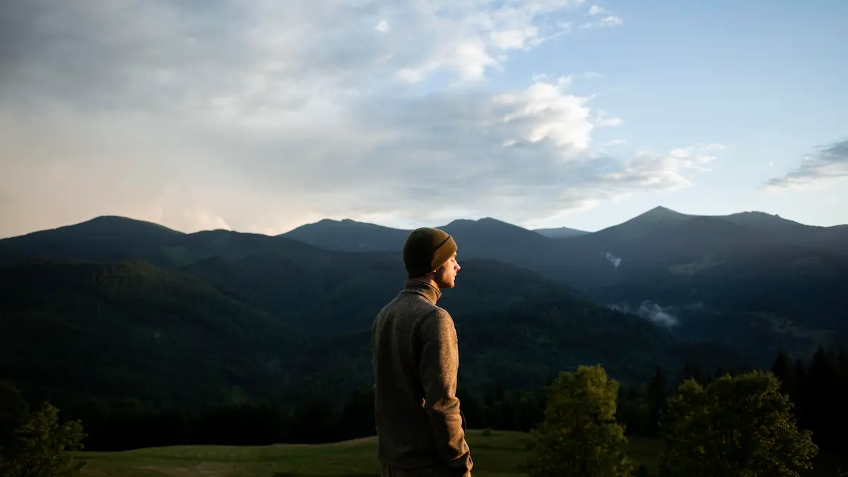 "Man standing in rural countryside with arms lifted in surrender, embracing peace and connection with God"
