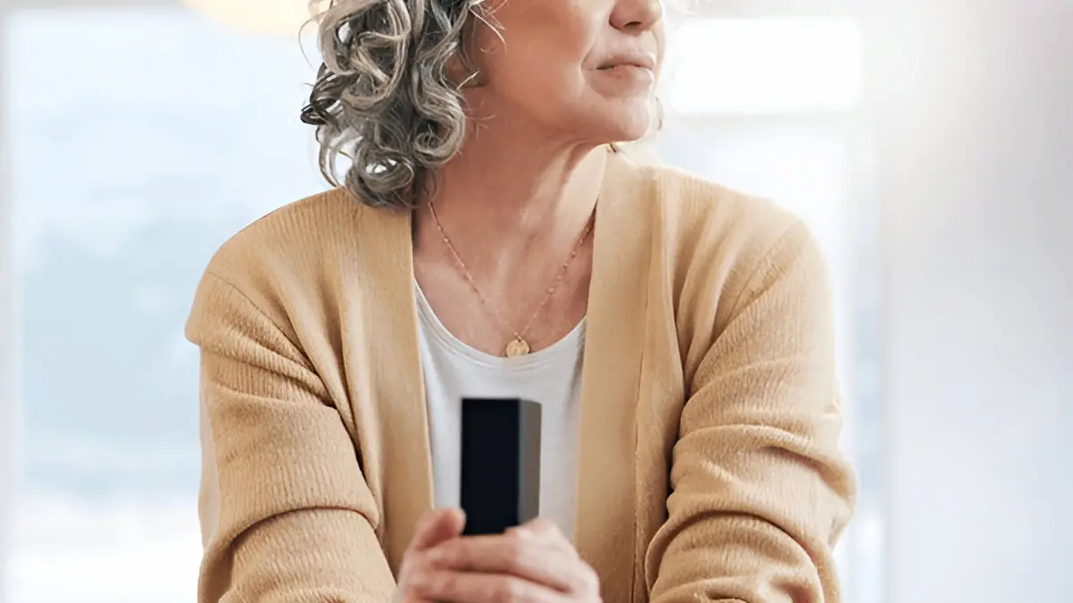 Woman in a beige sweater sitting calmly in prayerful reflection, symbolizing peace through faith.