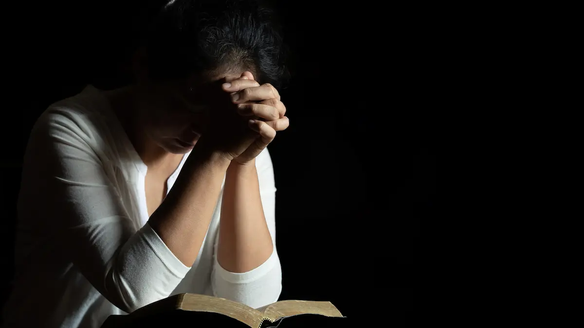 Person praying at midnight with bible on the laps