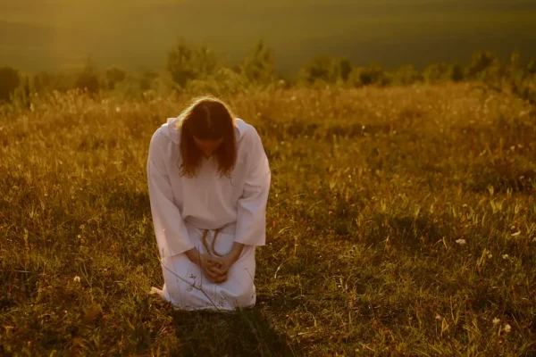A Christian kneeling in prayer at sunrise with an open Bible.