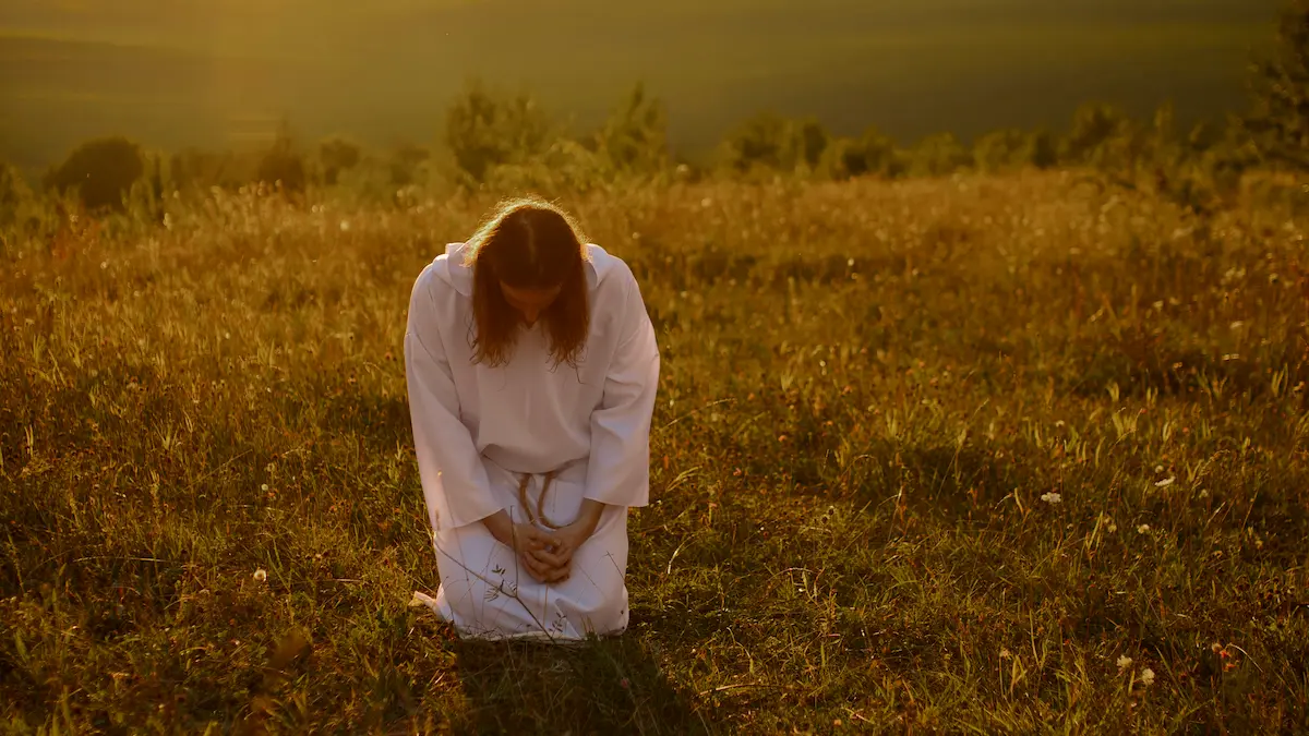 A Christian kneeling in prayer at sunrise with an open Bible.