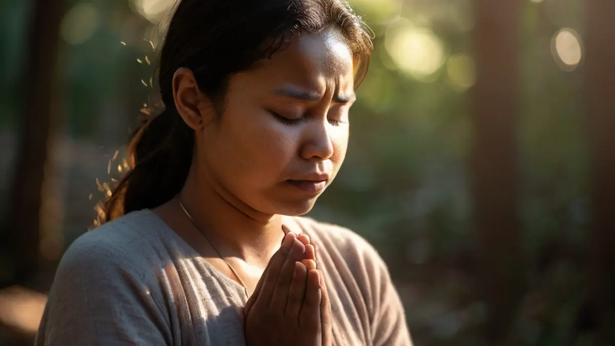Believer in prayer with eyes closed, hands lifted, light shining through window.